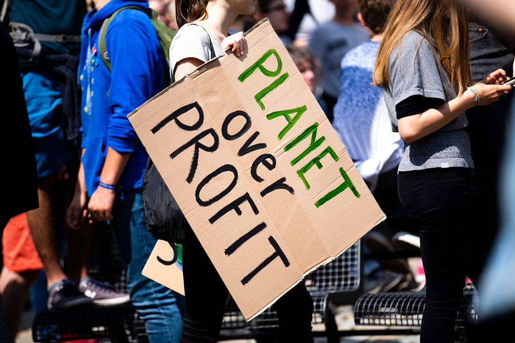 A person holds a protest sign that reads "planet over profit".